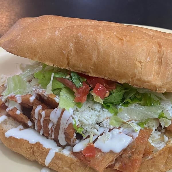 A Mexican torta sandwich filled with fried tortillas, lettuce, tomatoes, cheese, and crema.