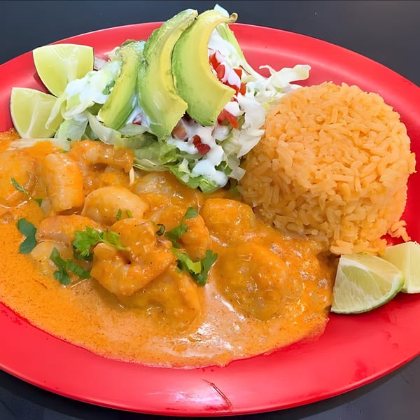Shrimp in orange sauce with rice, avocado, lettuce, and lime wedges on a red plate.