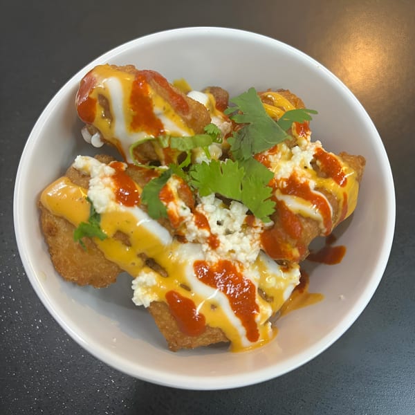 Crispy Mexican taquitos topped with queso, red sauce, sour cream, and cilantro in a white bowl.
