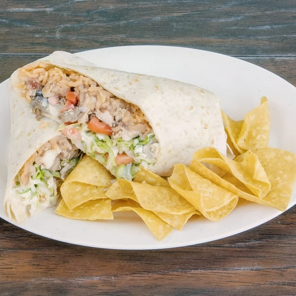 A large burrito, cut in half, revealing rice, meat, and vegetables, served with tortilla chips.
