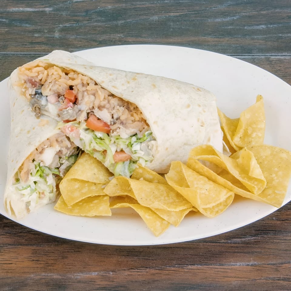 A large burrito, cut in half, revealing rice, meat, and vegetables, served with tortilla chips.