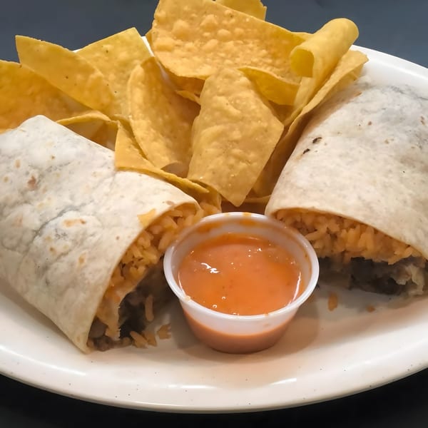 Two burritos with rice and meat, tortilla chips, and a side of orange sauce on a white plate.